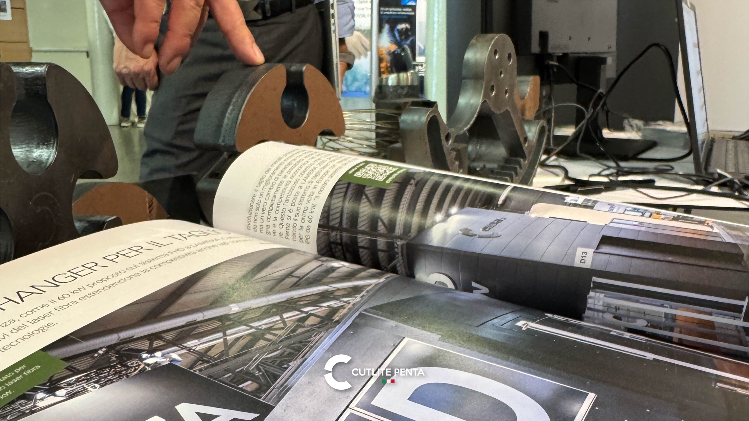 Dicke geschnittene Teile auf einem Tisch, daneben eine aufgeschlagene Fachzeitschrift mit einem Artikel über das auf der LAMIERA gezeigte FHD System mit 60 kW