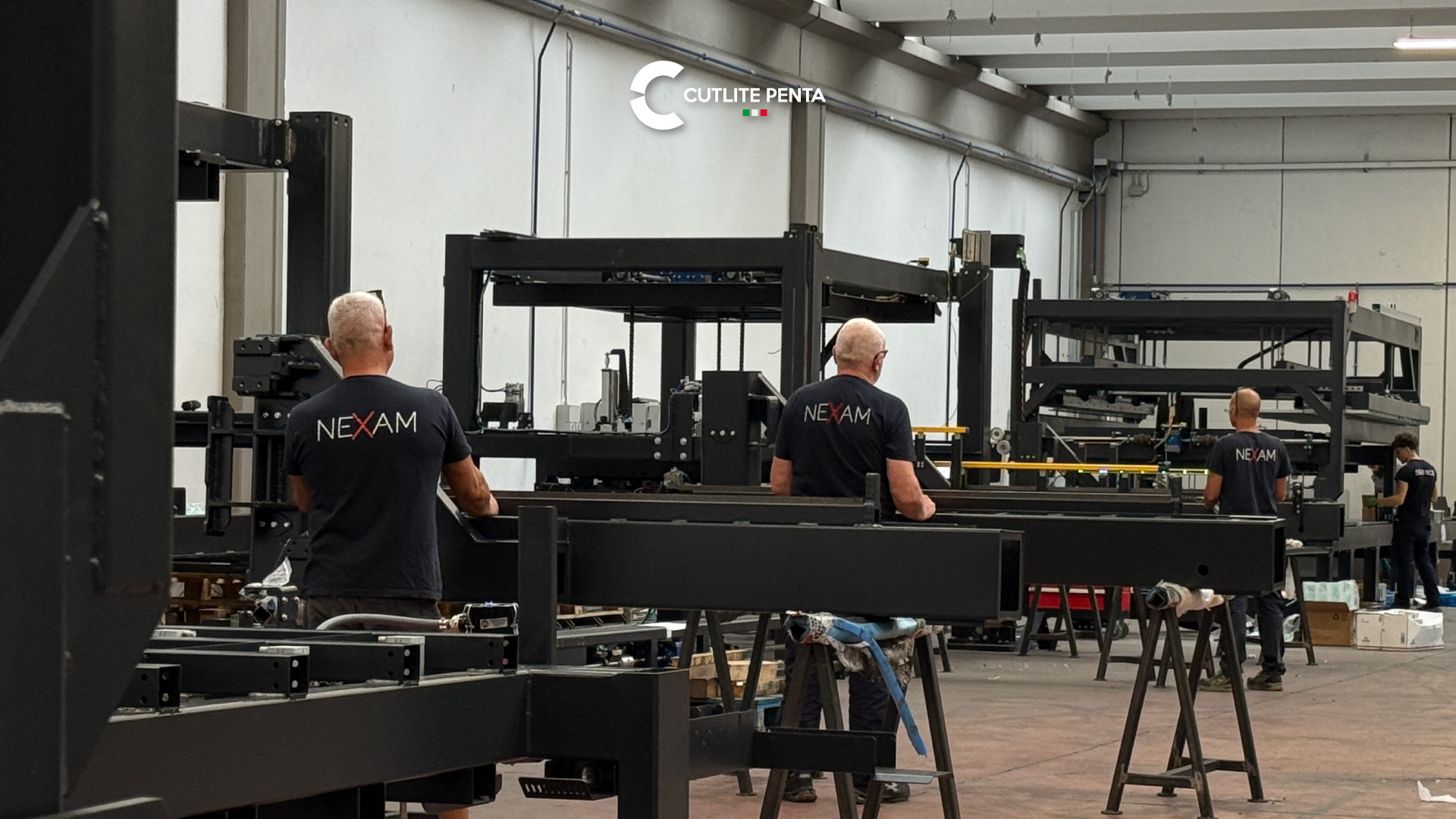 Drei Techniker in NEXAM-Shirts bei der Arbeit an den Stahlrahmen der automatischen Lager