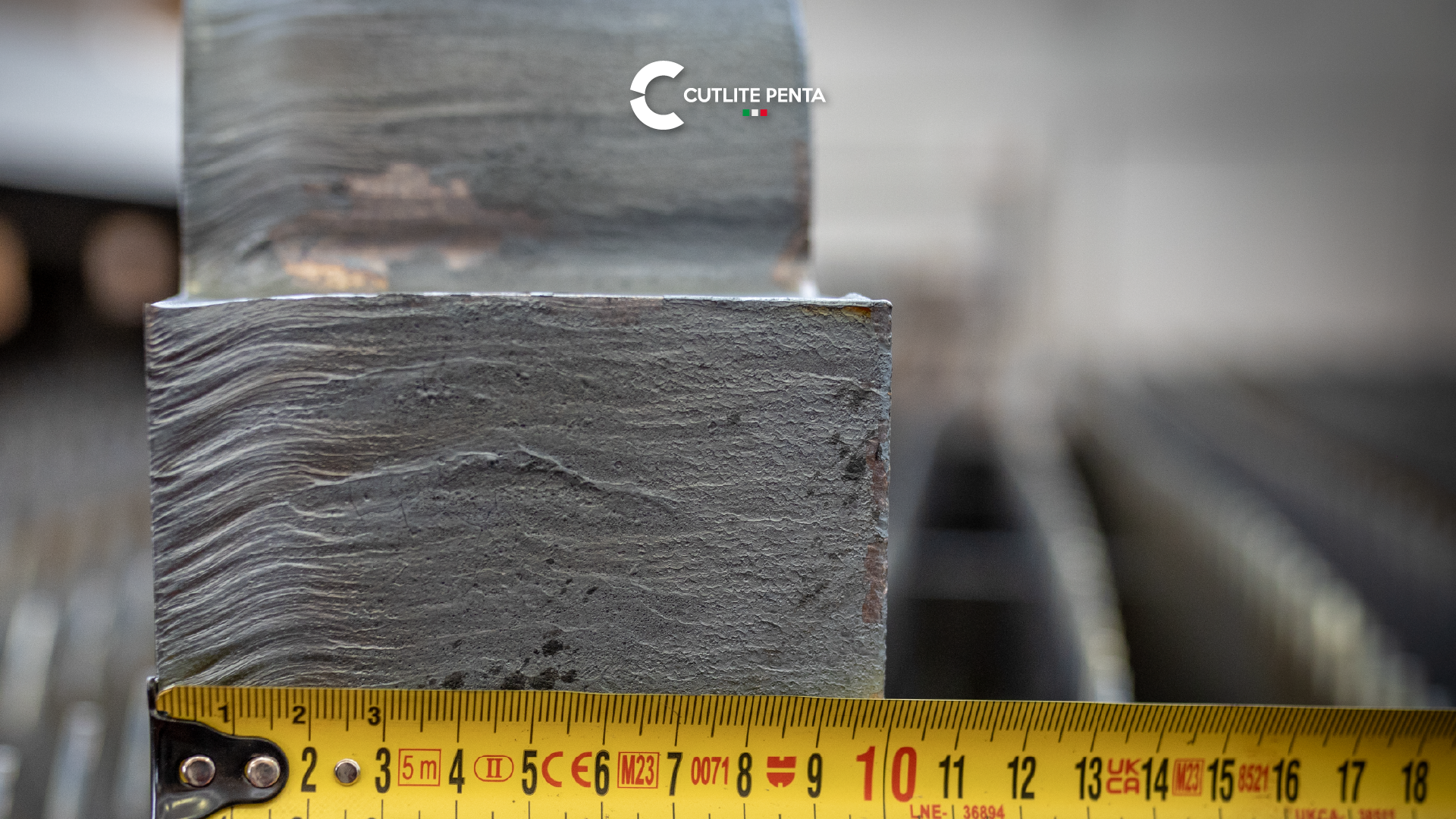 A heavy steel part held against a tape measure, with the cut face in full view