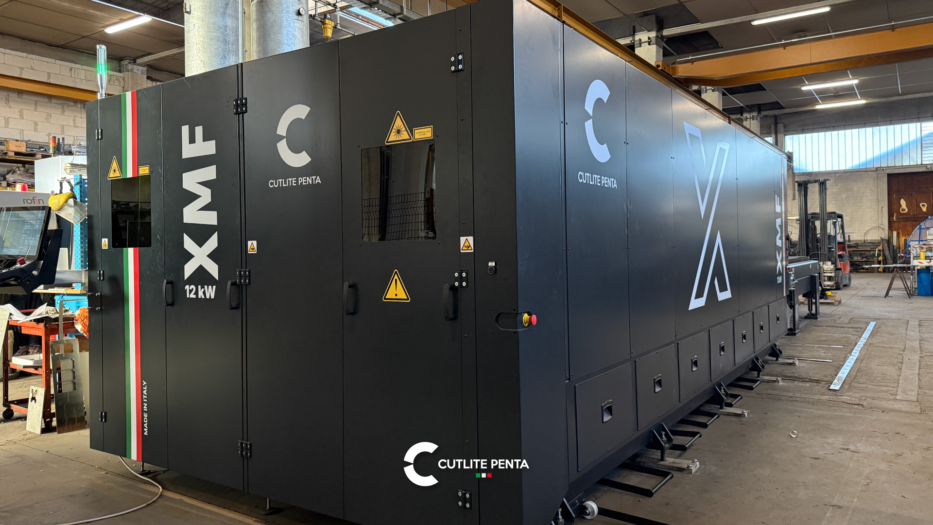 Gambuzzi's black XMF 12 kW with the Made in Italy tricolor stripe and, in the background, the old CO2 laser