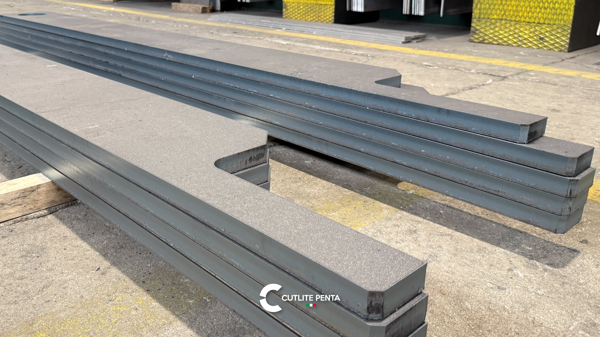 Long, thick laser-cut steel parts stacked in Tecnosider's yard