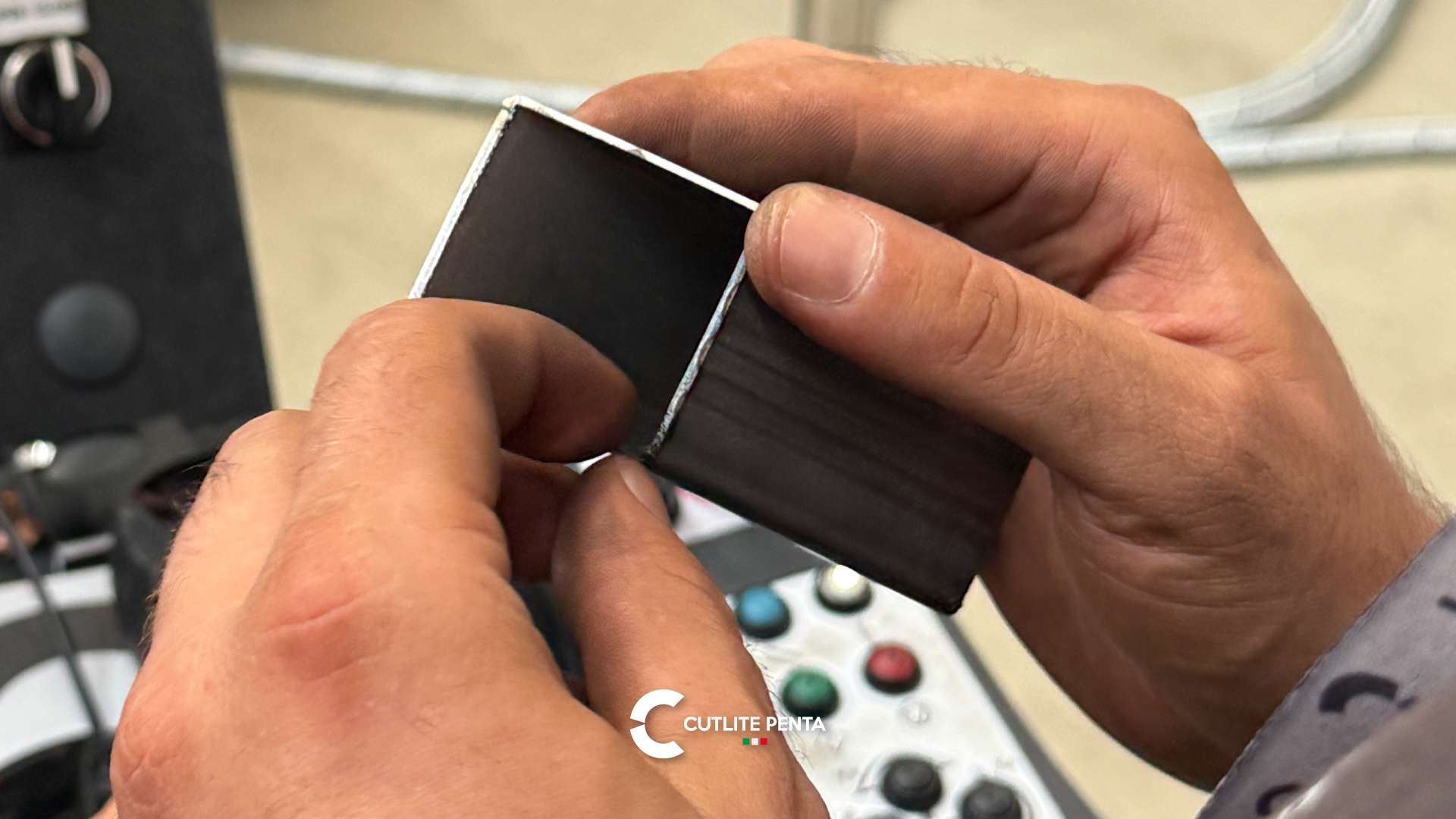 Mani che tengono un pezzo di tubo quadro tagliato al laser, davanti al pannello di comando di una macchina Cutlite Penta